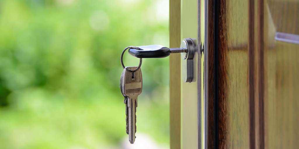 Door key hanging from the lock of a front door with blurred green foliage in the background