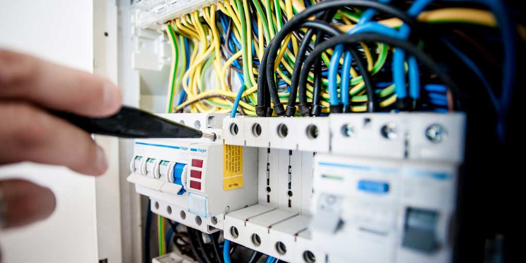 Close up of fuse switches in an electrical consumer unit, a hand is shown testing one of the fuses