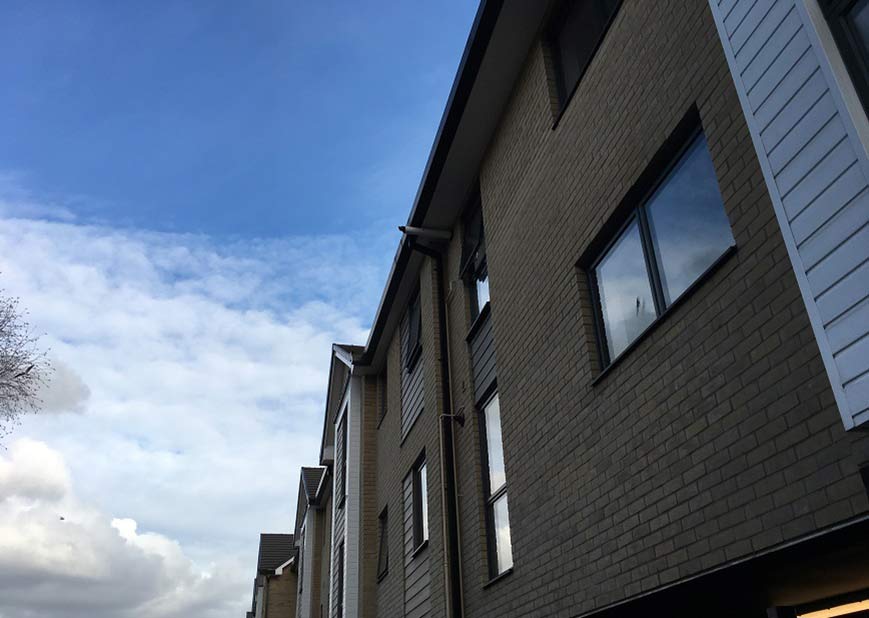 Looking up to a bright but cloudy sky, with a block of flats with cladding on parts of the front of the building on the right hand side